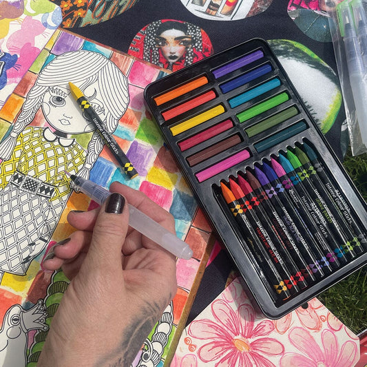 Intense Colour Caykes and Sticks - set 1 ... by Dyan Reaveley's Dylusions and Ranger. Tin of vibrant and watersoluble woodless watercolour (ink-based) pencils (sticks) and cylinder shaped pans (caykes), each in 12 (twelve) colours to use in watercolouring, painting, journaling, mixed media, visual arts of all kinds. Photo of Dyan's hand holding the Dylusions waterbrush colouring with the new paints.