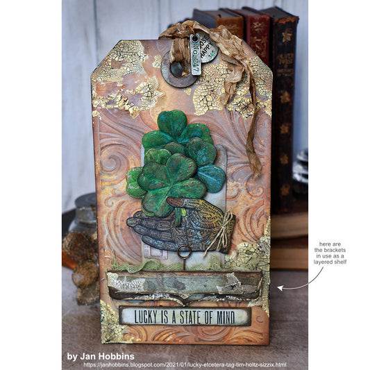 Bracket, Decorative Trims - Etcetera Thickboard Shapes ... by Tim Holtz and Stampers Anonymous. Packet of 3 (three) different lengths in 2 (two) different widths (5 of each size). THETC010. The Etcetera Bracket strips have a straight edge and shaped edge, as shown here in a large tag made by Jan Hobbins in 2021.
