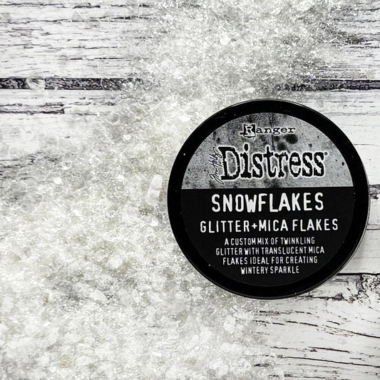 Snowflakes - Mica Flakes and Sparkly Dry Glitter ... by Tim Holtz Distress and Ranger. 3fl oz (88.7ml) jar. Made by Ranger. Tim Holtz Distress® Snowflakes combines a custom mix of twinkling glitter with translucent mica flakes for a nostalgic wintery sparkle.  Adhere Snowflakes with Distress Collage Medium, Ranger Glossy Accents, or other liquid adhesives. Photo from Ranger showing the contents on a wooden backdrop.