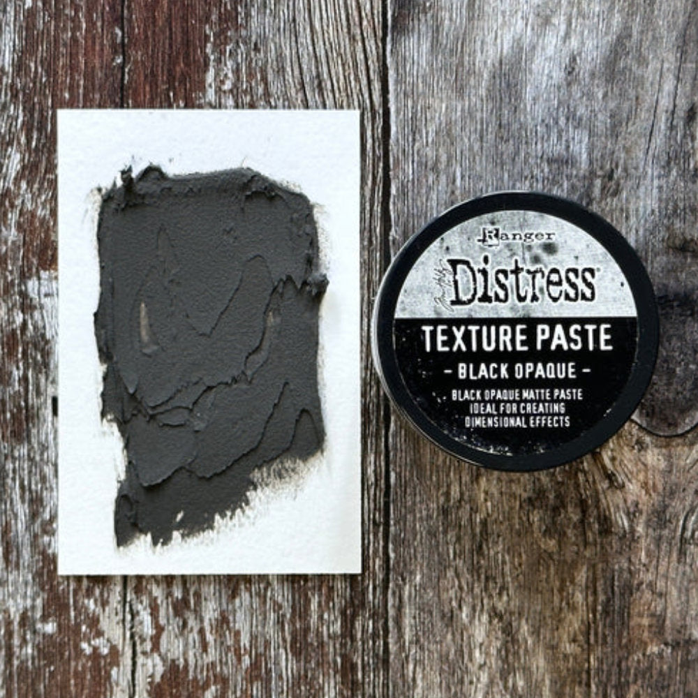 Black Texture Paste - Tim Holtz Distress Dimensional Medium with solid black coverage and matte finish, 3fl oz (88.7ml) jar. Made by Ranger. Tim Holtz Distress Texture Paste in Black is a dimensional medium that dries as you place it, with all the marks, peaks and effects you create. It is smooth dark sooty black medium which dries to an opaque (black) matte finish that is flexible and can be stained, die cut, trimmed, sanded, painted, or altered. Showing a sample made by Tim.