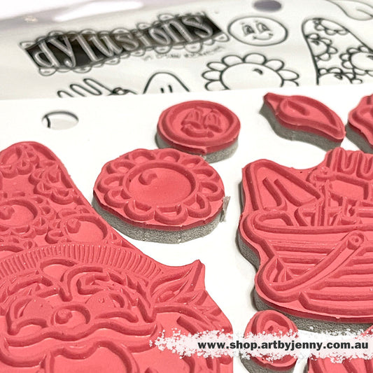Photo of Gnome Sweet Gnome Dylusions Stamp Set (DYR10011). Original designs by Dyan Reaveley, made by Stampers Anonymous out of red rubber mounted on cling foam. Perfect for mixed media, art journaling, scrapbooking, stamping on fabrics, using in papercrafts and visual arts of all kinds. 12 (twelve) designs.  These fun and whimsical designs include two large gnomes, a female and male, each standing tall and facing forwards, plus flowers, bucket and gardening tools, leaves, row of hearts and smiley faces.