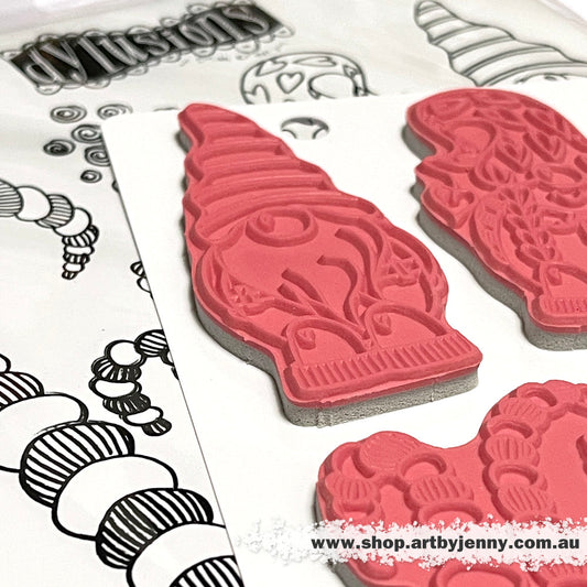 Photograph of the No Place Like Gnome Dylusions Stamp Set (DYR10008). Original designs by Dyan Reaveley, made by Stampers Anonymous out of red rubber mounted on cling foam. Perfect for mixed media, art journaling, scrapbooking, stamping on fabrics, using in papercrafts and visual arts of all kinds. 7 (seven) designs.  These fun and whimsical designs include three gnome friends (about 3" to 3.5" tall), with stripey swirly garden stalks (trees, grass, seaweed, hooks), spiral spots and little hearts.