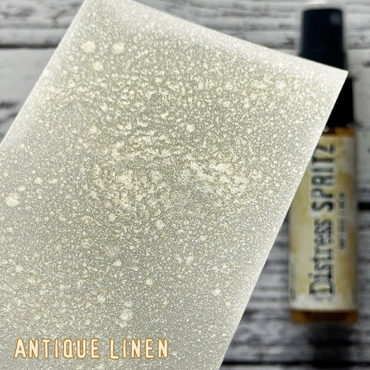 Antique Linen - Distress Spritz by Tim Holtz and Ranger - a pearlised fusion of colourful mica pigment and clear medium to easily create a gorgeous shimmery splattery effect on artwork in colours that compliment the whole Distress rainbow. Each bottle contains 1 fl oz (29ml) with a fine spritzing nozzle and easy to hold container. Use Tim Holtz Distress Spritz for mixed media, scrapbooking, paper crafts, card making, junk journals and visual arts. Photo is a sample by Ranger.