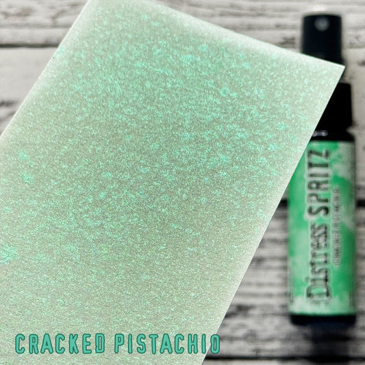 Cracked Pistachio - Distress Spritz by Tim Holtz and Ranger - a pearlised fusion of colourful mica pigment and clear medium to easily create a gorgeous shimmery splattery effect on artwork in colours that compliment the whole Distress rainbow. Each bottle contains 1 fl oz (29ml) with a fine spritzing nozzle and easy to hold container. Use Tim Holtz Distress Spritz for mixed media, scrapbooking, papercrafts, cardmaking, junk journals and visual arts. Photo is a sample by Ranger.