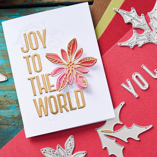 Seasonal Sketch - from the Vault ... Thinlits Die Cutting Templates by Tim Holtz, made by Sizzix (no.666719). These designs cut out an alphabet (uppercase condensed typeface with numbers and hashtag) and two Christmas themed foliage (poinsettia and holly). Photograph of a greeting card saying 'joy to the world' with layered poinsettia on white background with scraps around the table.