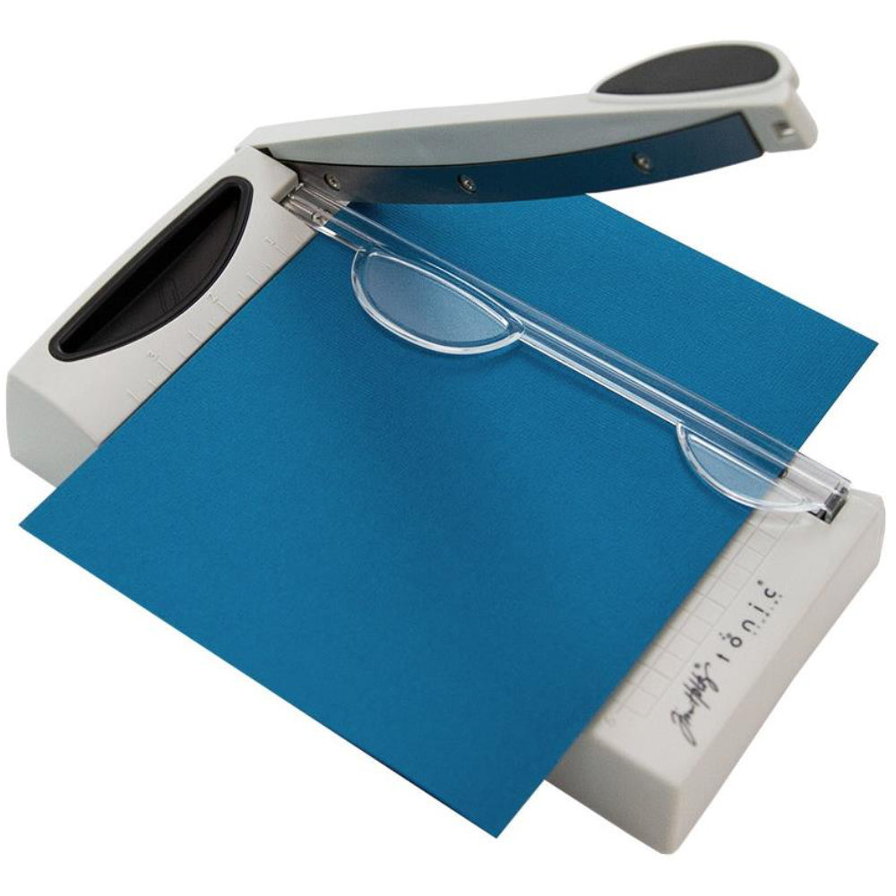 Mini Guillotine Trimmer - 6.25 inch with Comfort Kushgrip handle... by Tim Holtz and Tonic Studio. Portable guillotine, perfect for travelling to retreats, small storage spaces and saving room on tables! Has a sharp 22.5cm blade for use with paper and cardstock. Made by Tonic Studio with precision ground, ultra sharp blade, this strong trimmer is built to last. - image showing the portable cutting tool in use, trimming blue cardstock