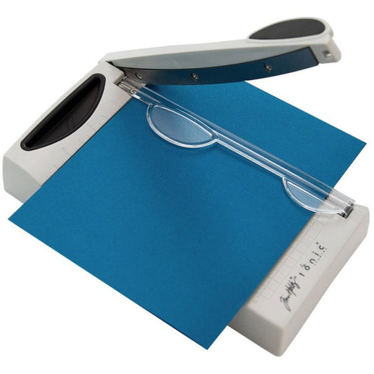Mini Trimmer - 6.25 inch Guillotine with Comfort Kushgrip handle by Tim Holtz and Tonic Studios. Portable guillotine, perfect for travelling to retreats, small storage spaces and saving room on tables! Has a straight sharp blade which cuts quietly and smoothly every time, for use with paper and cardstock. Made by Tonic Studio with precision ground, ultra sharp smooth quiet blade, this strong trimmer is built to last. Photo showing the tool in use.