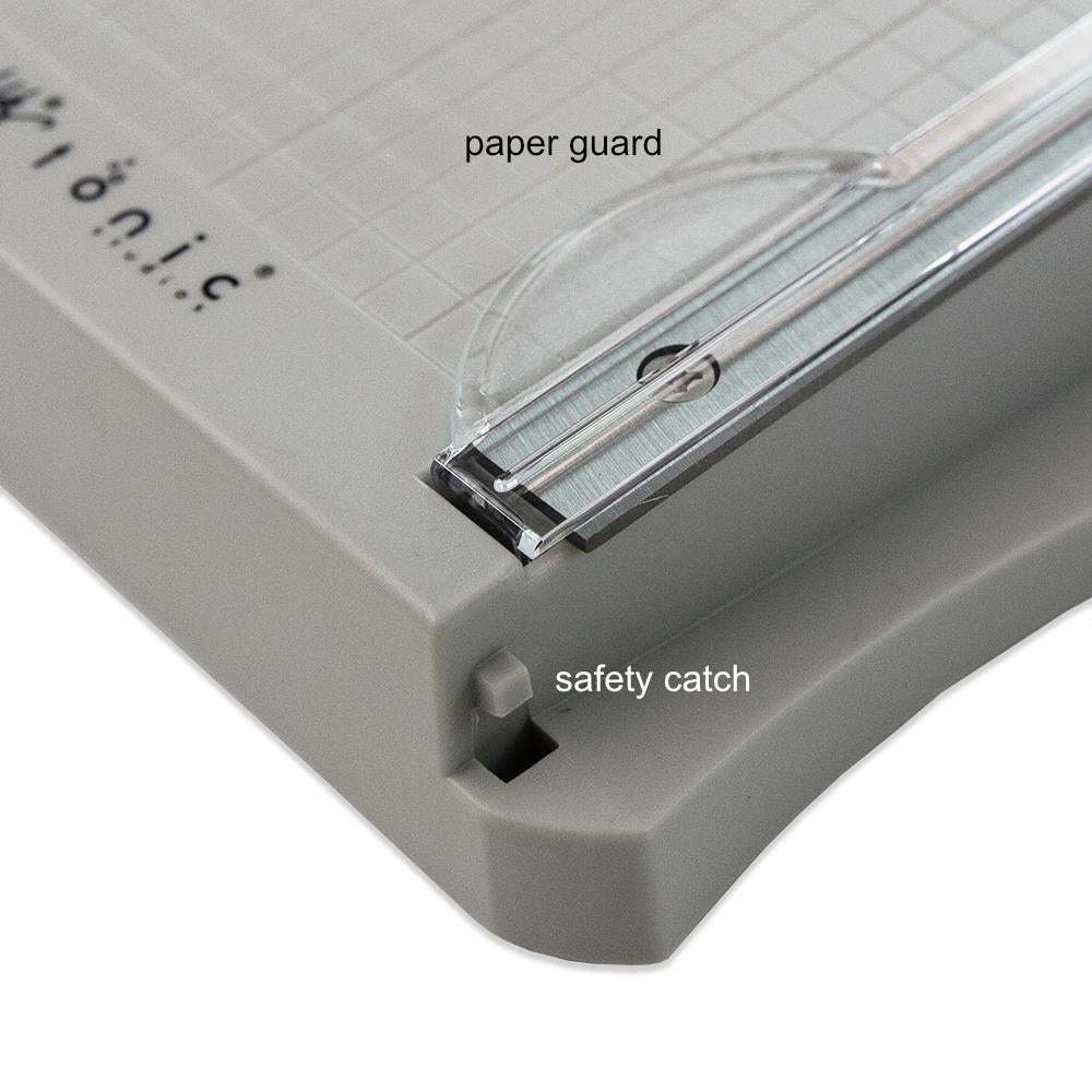 Mini Guillotine Trimmer - 6.25 inch with Comfort Kushgrip handle... by Tim Holtz and Tonic Studio. Portable guillotine, perfect for travelling to retreats, small storage spaces and saving room on tables! Has a sharp 22.5cm blade for use with paper and cardstock. Made by Tonic Studio with precision ground, ultra sharp blade, this strong trimmer is built to last. - image showing close up details of the blade safety catch and guard