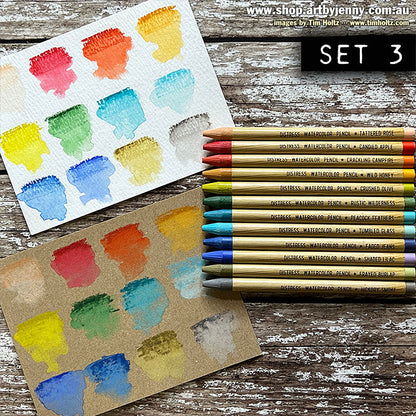 Distress Watercolour Pencils, set 3 ... by Tim Holtz. 12 (twelve) woodless watercolour pencils in Tattered Rose, Candied Apple, Crackling Campfire, Wild Honey, Crushed Olive, Rustic Wilderness, Peacock Feathers, Tumbled Glass, Faded Jeans, Shaded Lilac, Frayed Burlap, Hickory Smoke. One of each colour shown as swatches on kraft and watercolour paper