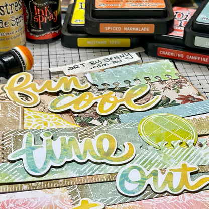 A close up photograph by Jenny James showing the 49 and Market paper embellishments called 'Irresistable' die cuts by Vicki Boutin. This photo shows the 'chipboard words' with strips from 'die cut borders', coloured using Distress and Dylusions inks to create customised scrapbooking layers for arts and crafts.