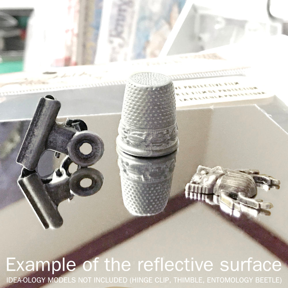 Mirrored Sheets ... Idea-Ology by Tim Holtz - adhesive backed sheets of highly reflective material that can be cut or used whole, for use as embellishments for scrapbooking, papercrafts, craft decor, display makes, creative visual arts and mixed media projects (TH93029). 2 (two) sheets, each 6" x 9" (15cm x 23cm). Use this mirrored surface to create miniature mirrors, silver trays, reflective element in your artwork. Photograph unedited, showing the mirrored sheet reflecting a metal clip, thimble and bug.