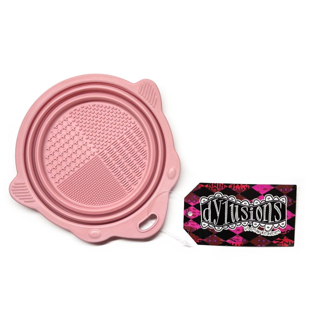 Pink Collapsible Brush Cleaning Bowl - Designed by Dyan Reaveley for Dylusions and Ranger. To use, pull the sides up to create a bowl. Pour in your water or brush cleaner. Swish your brushes around using the textured plate on the base to encourage the bristles to release the paint. Wipe off the brush with your painting rag. Ue the shaped sides to lean a brush so it doesn't roll away. Photo of the bowl flat, closed.