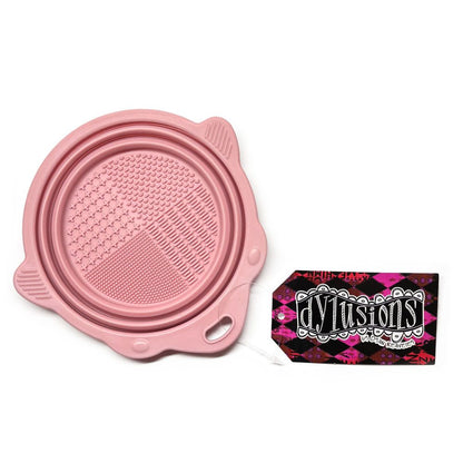 Pink Collapsible Brush Cleaning Bowl - Designed by Dyan Reaveley for Dylusions and Ranger. To use, pull the sides up to create a bowl. Pour in your water or brush cleaner. Swish your brushes around using the textured plate on the base to encourage the bristles to release the paint. Wipe off the brush with your painting rag. Ue the shaped sides to lean a brush so it doesn't roll away. Photo of the bowl flat, closed.