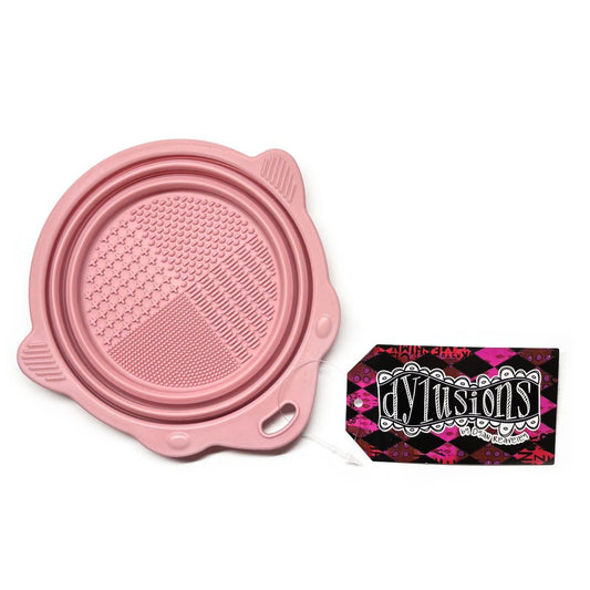 Pink Collapsible Brush Cleaning Bowl - Designed by Dyan Reaveley for Dylusions and Ranger. To use, pull the sides up to create a bowl. Pour in your water or brush cleaner. Swish your brushes around using the textured plate on the base to encourage the bristles to release the paint. Wipe off the brush with your painting rag. Ue the shaped sides to lean a brush so it doesn't roll away. Photo of the bowl flat, closed.