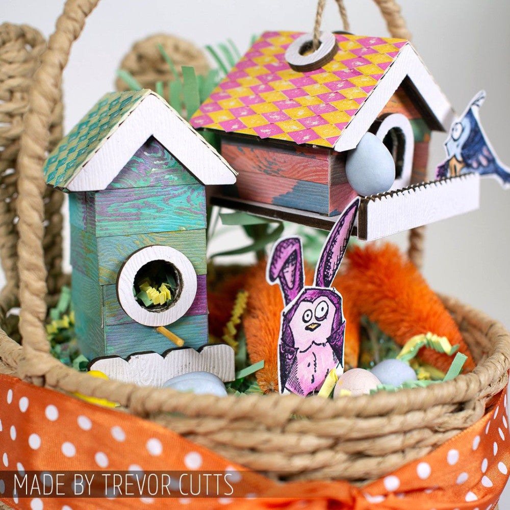 Birdhouse Ornaments - Thickboard Shapes by Stampers Anonymous. 2 (two) sheets of compressed board with precut designs of little bird house pieces, ready to pop out and use to create 4 (four) house faces, 2 short and 2 tall. 18 pieces per sheet. ORN01  Each sheet is 4 1/2" x 6 3/4" and approx 2mm thick. Photograph of two birdhouses in a basket, made using this kit with additional pieces to create whole boxes with roof tiles. Made by Trevor Cutts of Stampers Anonymous.