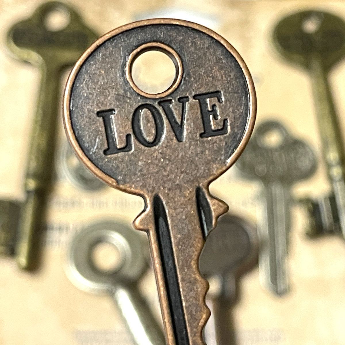 Word Keys, Metal Adornments&nbsp;... by Tim Holtz Idea-Ology - Solid metal keys inspired by vintage keys, each in a different shape and style, engraved with heartfelt words. Use for mixed media, assemblage projects, off-the-page marvels and party decor. 7 (seven) pieces, 1 (one) of each design. TH92680. uniquely shaped embellishment with words of : love, secret, life, memory, journey, dreams, heart. Photo of 'love'