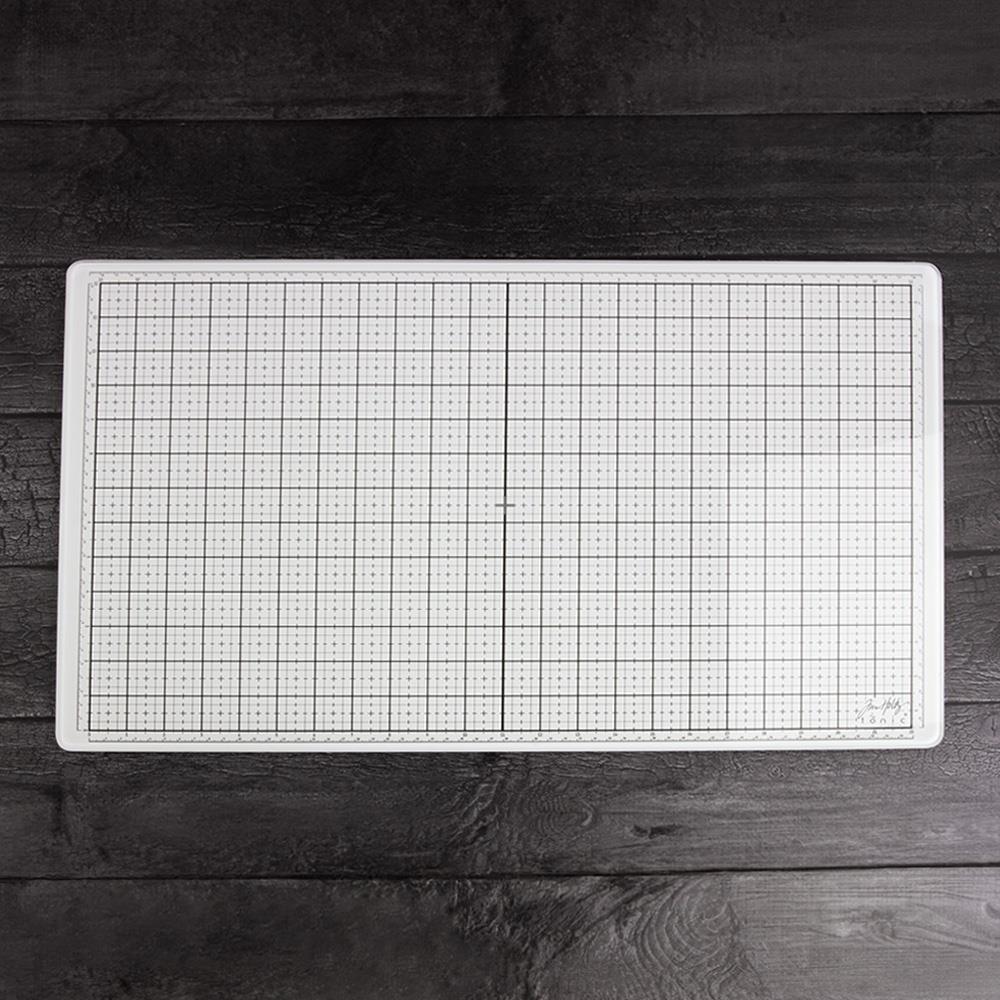 White Studio Glass Media Mat - Large Creative Surface 14"x23" ... by Tim Holtz and Tonic Studios. A bright white tempered glass mat with gridlines, silicon feet with both metric and imperial measurements marked around all the edge. Photograph showing the top surface of the glass mat on a timber tabletop background.