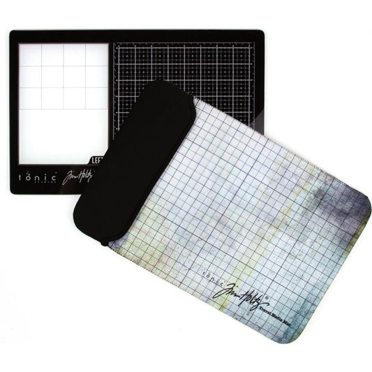 Black Travel Sized Glass Media Mat with Storage Pouch - by Tim Holtz and Tonic Studios ... a portable handy size tempered glass craft surface 10 1/4" x 15 3/4" (26cm x 40cm) - black glass mat with white gridlines and rectangle white area for mixing plus nonstick Removable Palette. Labelled "left handed" as the white mixing area is on the left hand side. The perfect size for retreats, holidays, the lounge room, taking to work, small craft corners, studios, anywhere you wish. Photo of the mat and pouch.