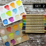 Distress Watercolour Pencils, set 2 ... by Tim Holtz. 12 (twelve) woodless watercolour pencils in Kitsch Flamingo, Barn Door, Spiced Marmalade, Fossilized Amber, Twisted Citron, Cracked Pistachio, Mermaid Lagoon, Iced Spruce, Prize Ribbon, Seedless Preserves, Antique Linen, Vintage Photo. One of each colour shown as swatches on both kraft and white paper.