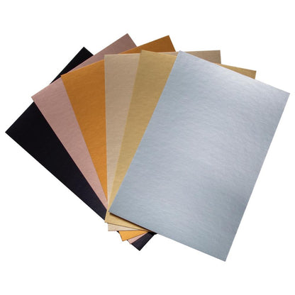 Photograph of the Metallic Classics - Kraft Stock Cardstock Idea-Ology Paper by Tim Holtz. Sheets of shiny smooth cardstock in gorgeous traditional metallic colours on Kraft (natural tan, brown) core. 24 Sheets, 6 Colours (4 of each) with a smooth very shiny finish. Sheet size is 6"x9" (15.24cm x 22.86cm). The top surface are coated with high gloss metallic shiny finish in the 'go with everything' colours of black, silver, gold, pewter, rose gold and copper. 